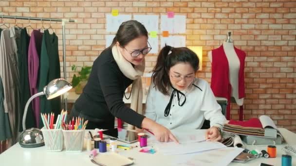 亚洲中年女性时装设计师在工作室教一位年轻的受训者裁缝用彩线和缝纫面料设计服装 专业精品小生意 — 图库视频影像