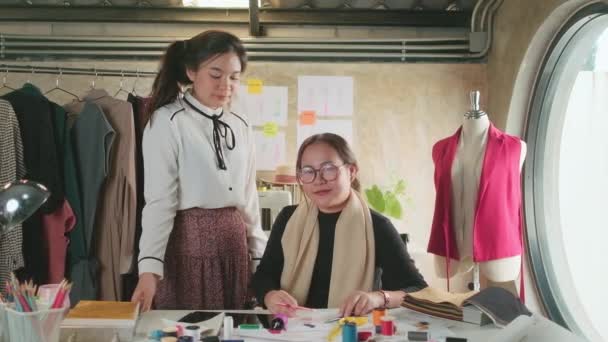 ファッションチーム アジアの女性デザイナーとスタジオで10代のアシスタント 腕が交差し ドレスデザインのためのカラフルな糸と縫製で幸せな作業 プロのブティックテーラー中小企業起業家 — ストック動画