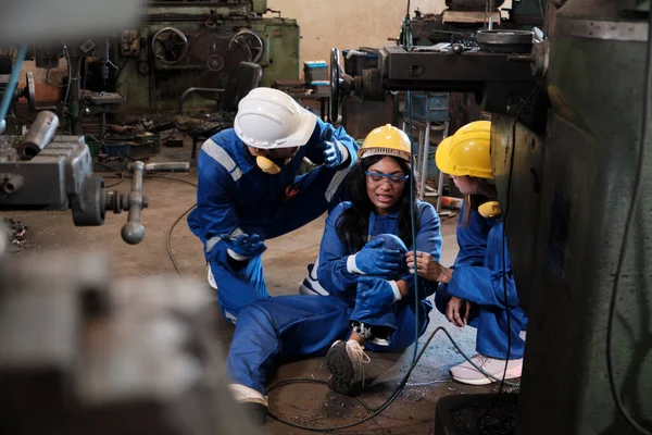 Painful accident in industrial production metalwork, African American female worker injured her leg, male engineer and colleague team helped first aid with care at manufacturing machinery factory.