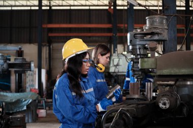 Koruyucu ve güvenlik üniformaları ve şapka giyen bir endüstri işçileri ekibi, erkek yönetici ve bayan meslektaşlar fabrikada metal fabrikalarında çalışıyor. Profesyonel üretim mühendisi.