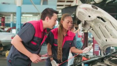 Male professional automotive supervisor advises and inspects Black female mechanic worker about liquid engine oil at car garage, service maintenance, and fixing specialist occupations auto industry.