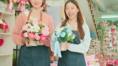 Two cheerful female florist workers give beautiful flora bouquets and look at camera together, happy and bright smiles, arranging work in a colorful flower shop, SME business entrepreneur people. 
