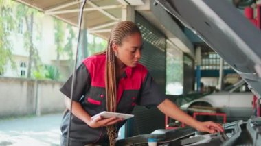 One Black female professional automotive mechanical worker checks an EV car battery and hybrid engine at a maintenance garage, expert electric vehicle service, and fixing occupations auto industry.
