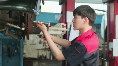 One young expert Asian male automotive mechanic technician is screwing car wheel nuts on lifting with wrench for repair at garage. Vehicle maintenance service works, industry occupation business jobs.