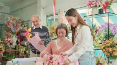 Flower shop team, Young beautiful female florist workers with old owner arranging and decorating bunch of fresh blossoms, smiling with happy work in colorful store, small business SME entrepreneur. 