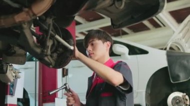 Genç bir Asyalı erkek otomotiv teknisyeni garajda tamir için ingiliz anahtarıyla kaldırma konusunda araba tekerleği delisi beceriyor. Araç bakımı işleri, endüstriyel meslekler.