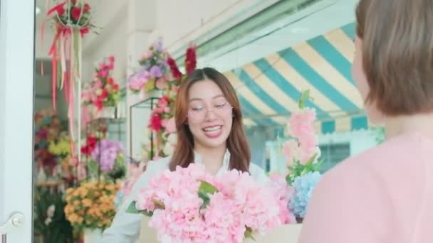 若いアジアの女性花屋の労働者は 注文を購入した顧客に新鮮な花を提供します スマートフォンアプリケーションによるキャッシュレス支払い カラフルな花の店で幸せな仕事 中小企業起業家 — ストック動画