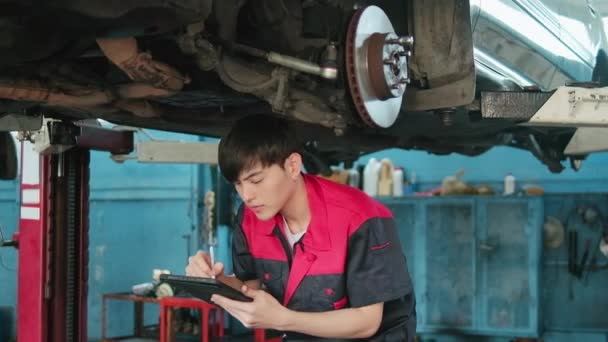 Professional Young Asian Male Motor Mechanic Inspects Undercarriage Electric Car — Wideo stockowe