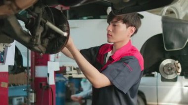 One young expert Asian male automotive mechanic technician is screwing car wheel nuts on lifting with wrench for repair at garage. Vehicle maintenance service works, industry occupation business jobs.