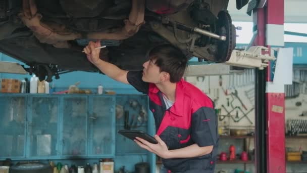 Professional Young Asian Male Motor Mechanic Inspects Undercarriage Electric Car — Wideo stockowe