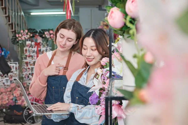 Two young beautiful female florist partners decorate lovely flora bunch for online purchase orders and website arrangement for business, happy work in colorful flower shop store, and e-commerce SME.