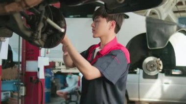 One young expert Asian male automotive mechanic technician is screwing car wheel nuts on lifting with wrench for repair at garage. Vehicle maintenance service works, industry occupation business jobs.