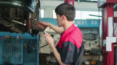 One young expert Asian male automotive mechanic technician is screwing car wheel nuts on lifting with wrench for repair at garage. Vehicle maintenance service works, industry occupation business jobs.