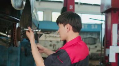One young expert Asian male automotive mechanic technician is screwing car wheel nuts on lifting with wrench for repair at garage. Vehicle maintenance service works, industry occupation business jobs.