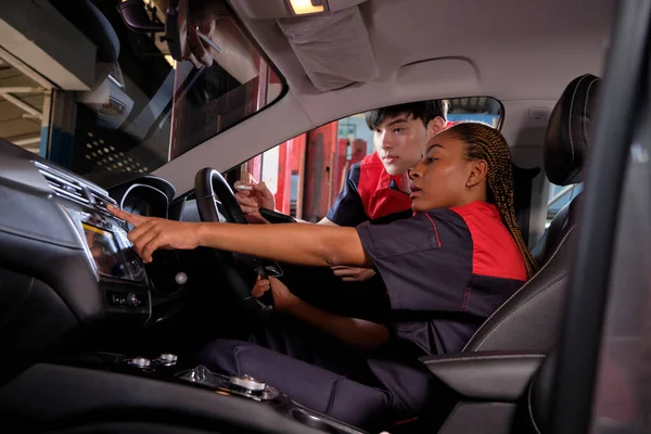 Genç siyahi kadın otomotiv teknisyeni ve partneri bakım listesini garajın içinde tabletle kontrol ediyorlar. Araç servisi tamir ve onarım işleri, endüstriyel meslekler.