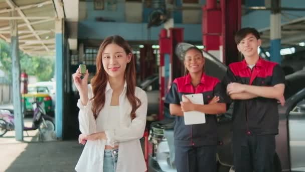 年轻的亚洲女性客户与汽车修理工们一起展示汽车钥匙 在维修车间 专业汽车服务中心 修整汽车工业等地愉快地微笑着对质量的信任 — 图库视频影像