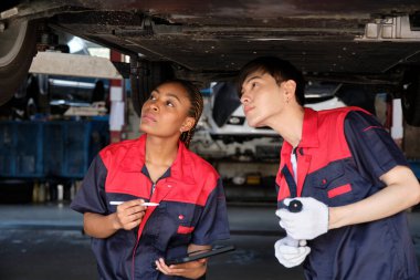 İki profesyonel otomotiv işçisi, kaldırılmış elektrikli arabanın mekanik kontrol şasisi, bakım garajında tamir ve onarım konularını ve uzman hizmet sektörü mesleğini tartışıyor..