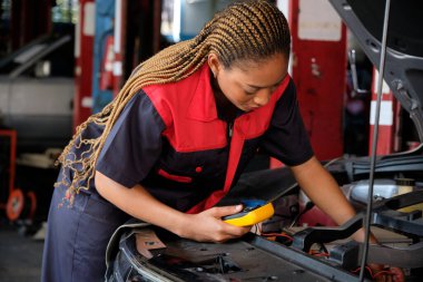 Siyahi bir kadın otomotiv işçisi bakım garajında bir EV araba aküsü ve hibrit motoru kontrol ediyor, uzman elektrikli taşıt servisi ve otomobil sektörünü tamir ediyor..