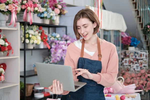 Stock image Portrait of one young White female florist owner in apron with laptop in bright and beautiful flower shop store smiles with online shopping jobs, small e-commerce business, happy SME entrepreneur. 