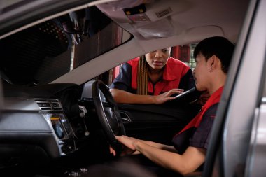 Genç Asyalı erkek otomotiv teknisyeni ve partneri bakım listesini garajın içinde tabletle kontrol ediyor. Araç servisi tamir ve onarım işleri, endüstriyel meslekler.