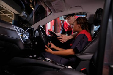 Genç siyahi kadın otomotiv teknisyeni ve partneri bakım listesini garajın içinde tabletle kontrol ediyorlar. Araç servisi tamir ve onarım işleri, endüstriyel meslekler.