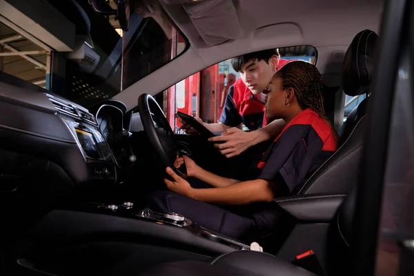 stock image Young Black woman automotive mechanic technician and partner checking maintenance list with tablet in car interior at garage. Vehicle service fix and repair works, industrial occupation business jobs.