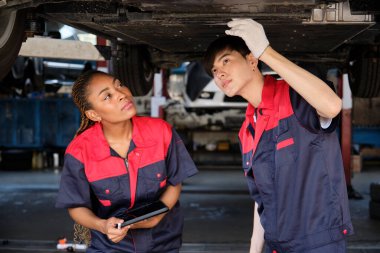 İki profesyonel otomotiv işçisi, kaldırılmış elektrikli arabanın mekanik kontrol şasisi, bakım garajında tamir ve onarım konularını ve uzman hizmet sektörü mesleğini tartışıyor..