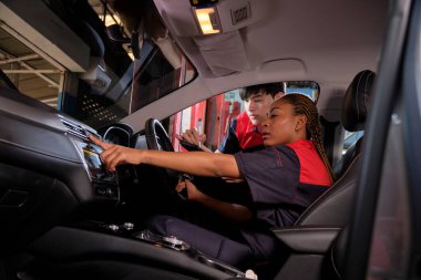 Genç siyahi kadın otomotiv teknisyeni ve partneri bakım listesini garajın içinde tabletle kontrol ediyorlar. Araç servisi tamir ve onarım işleri, endüstriyel meslekler.