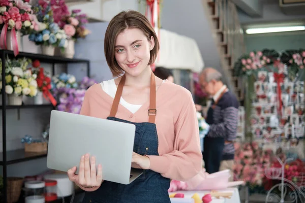 stock image Portrait of one young White female florist owner in apron with laptop in bright and beautiful flower shop store smiles with online shopping jobs, small e-commerce business, happy SME entrepreneur. 