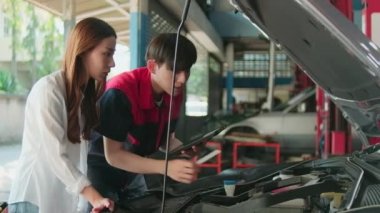 Erkek otomotiv işçisi Asyalı müşterilere kontrol listesi, EV araba tamiri ve bakım garajındaki hibrit motor, uzman elektrikli araç servisi ve meslek otomobil tamiri konularını açıklıyor..