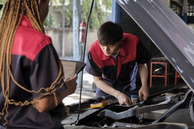 Two professional automotive mechanical partners check and repair an EV car battery and hybrid engine at a maintenance garage, expert electric vehicle service, and fixing occupations auto industry.