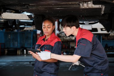 İki profesyonel otomotiv işçisi, kaldırılmış elektrikli arabanın mekanik kontrol şasisi, bakım garajında tamir ve onarım konularını ve uzman hizmet sektörü mesleğini tartışıyor..
