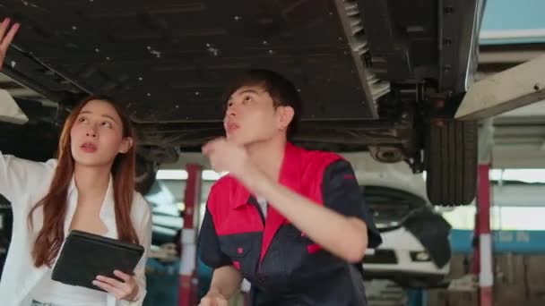 アジアの女性自動車ビジネス起業家は 男性の機械労働者と議論します 解除された電気自動車のチェックリストの馬車 メンテナンスガレージでの修理や修理 自動車サービスの仕事業界 — ストック動画