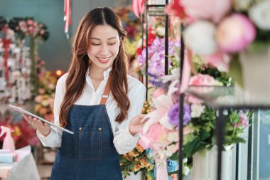 Parlak ve güzel çiçekçi dükkanında tabletle önlüklü güzel bir Asyalı kadın çiçekçinin portresi. İnternet üzerinden E-ticaret, küçük işletme işi, mutlu KME girişimcisi..