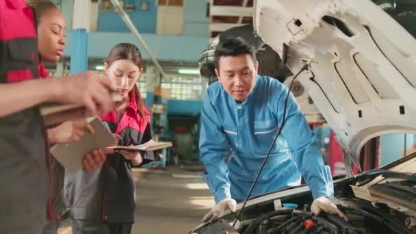 アジアの男性プロの自動車エンジニアの監督者は 修理サービスガレージ 自動車業界の専門職業の修理サービスのスタッフチームと車のエンジンのメンテナンスや修理作業を説明します — ストック動画