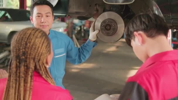 アジアの男性プロの自動車エンジニアの監督者は 修理サービスガレージ 自動車業界の専門職業で整備士の労働者チームと車のホイールとサスペンション修理作業を説明します — ストック動画