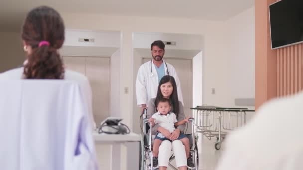 入院診療所での診察 国民健康診断 受診予約などのために車椅子で少年をからかう制服姿の幸せな若い女性小児科医 — ストック動画