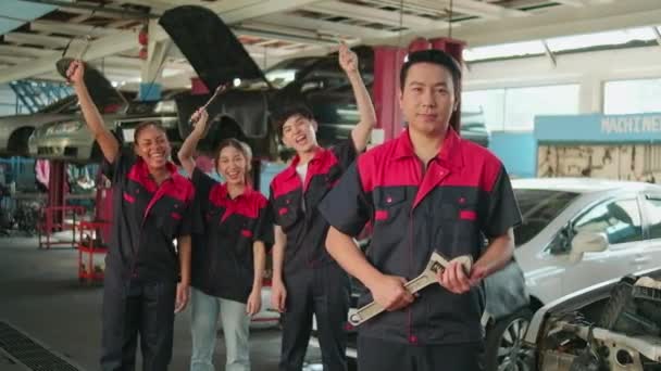 プロの労働者チームの面白い肖像画 男性監督者の腕は サービスガレージで明るい笑顔で車の修理の仕事の成功を祝う 整備士の同僚の前で固定ツールと交差 — ストック動画