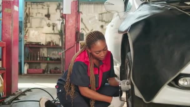 黒の女性の自動車整備士の労働者は ガレージでの修理のためのレンチと車のホイールナットをネジ 車両整備サービスの仕事 産業職業ビジネス 幸せな労働仕事 笑顔と陽気な — ストック動画