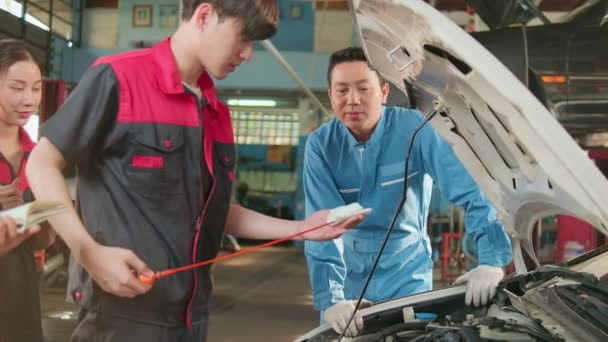 アジアの男性専門家の自動車監督者は 自動車ガレージ サービスメンテナンス および固定専門職業自動車業界での液体エンジンオイルに関する整備士の労働者に助言 および検査を行います — ストック動画