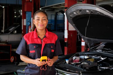 Siyahi bir kadın otomotiv işçisi bakım garajında bir EV araba aküsü ve hibrit motoru kontrol ediyor, uzman elektrikli taşıt servisi ve otomobil sektörünü tamir ediyor..