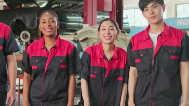 多种族专业技工团队在下班后庆祝汽车修理工作的成功 带着愉快的笑容用固定工具举手 并在服务性汽车修车厂看着相机 — 图库视频影像