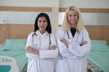 Profesyonel sağlık personeli partnerleri, iki üniformalı kadın doktor kameraya bakıyor, neşeli ve kollarını kavuşturmuş, hastane kliniğinde mutlu fiziksel işler yapıyorlar.. 