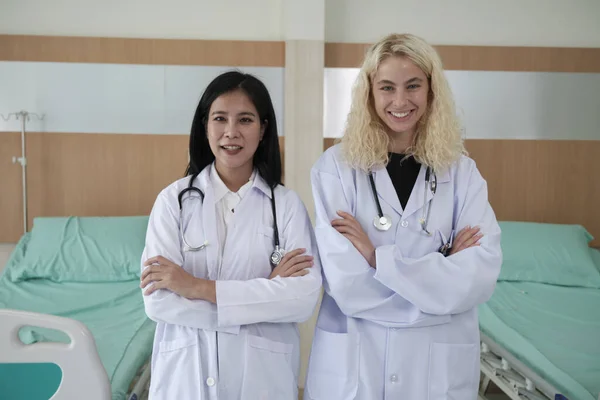 Professional medical staff partners, two uniformed female doctors look at camera, cheerful and arms crossed, happy physical work occupation in hospital clinic.