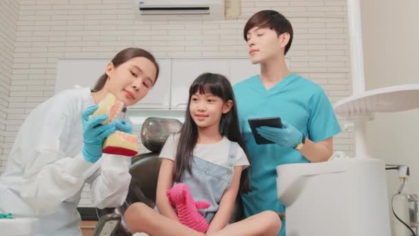 アジアの女性小児科歯科医とアシスタントは 歯科診療所 健康衛生 および腎臓病院でのプロの矯正医療の仕事で歯ブラシを示しています — ストック動画