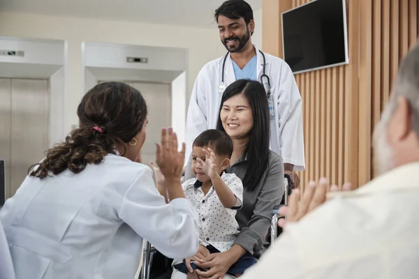 Happy young female pediatric doctor in uniform teasing little boy in wheelchair for medical exam at outpatient clinic hospital, people public health care checkup, and appointment visit.