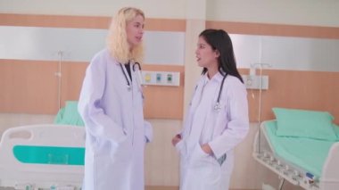 Profesyonel tıp personelinin portresi, iki üniformalı kadın doktor birlikte konuşuyor, kameraya bakıyor ve gülümsüyor, hastane kliniğinde mutlu fiziksel işler yapıyor..