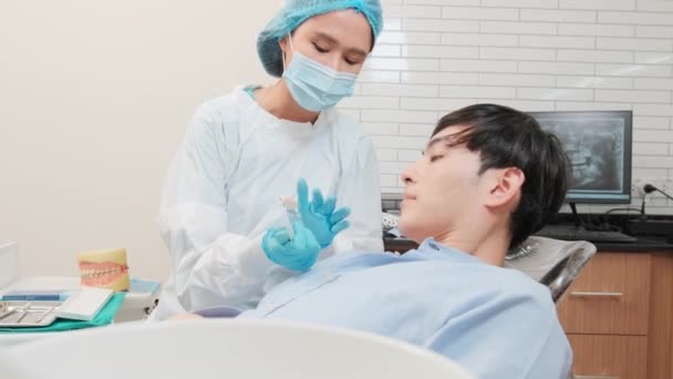アジアの女性歯科医は 歯科医院 歯科衛生医師 病院の専門医療で歯の色合いを有する若い男性患者に矯正ケアの仕事とホワイトニングを説明します — ストック動画