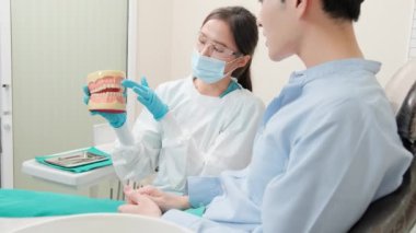 Asyalı kadın dişçi diş sağlığı kliniğinde diş modeli olan genç erkek hastaya diş bakımını ve beyazlatmayı, sağlık bakımını ve doktorluk hastanesinde profesyonel sağlık hizmetlerini anlatıyor..