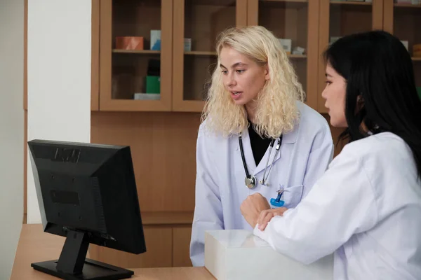 Two professional medical staffs, Asian female doctor, and White pharmacist discussed treatment medicine prescriptions at counter of the pharmacy department in hospital clinic.